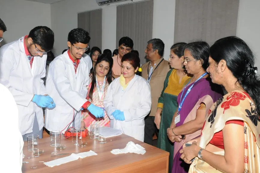 Two young men wearing safety glasses and white coats conduct an experiment using coins