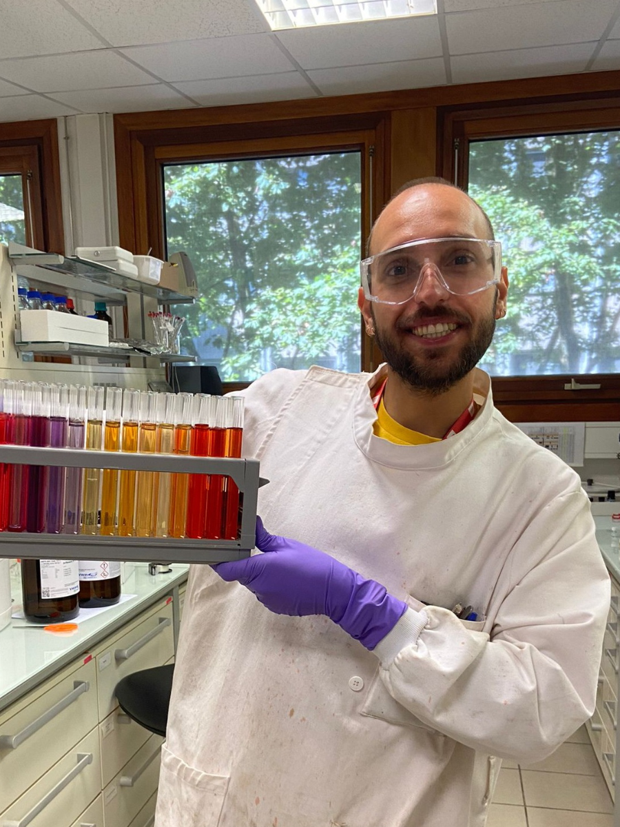 One of the PISCO Team in a lab coat and gloves holding test tubes with coloured liquids in