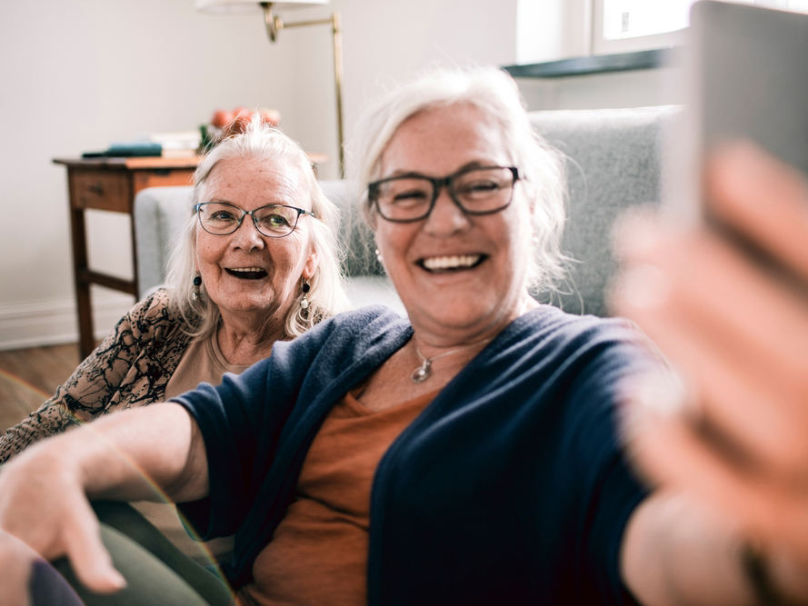 Close up of two senior ladies using a phone to take selfie in the living room