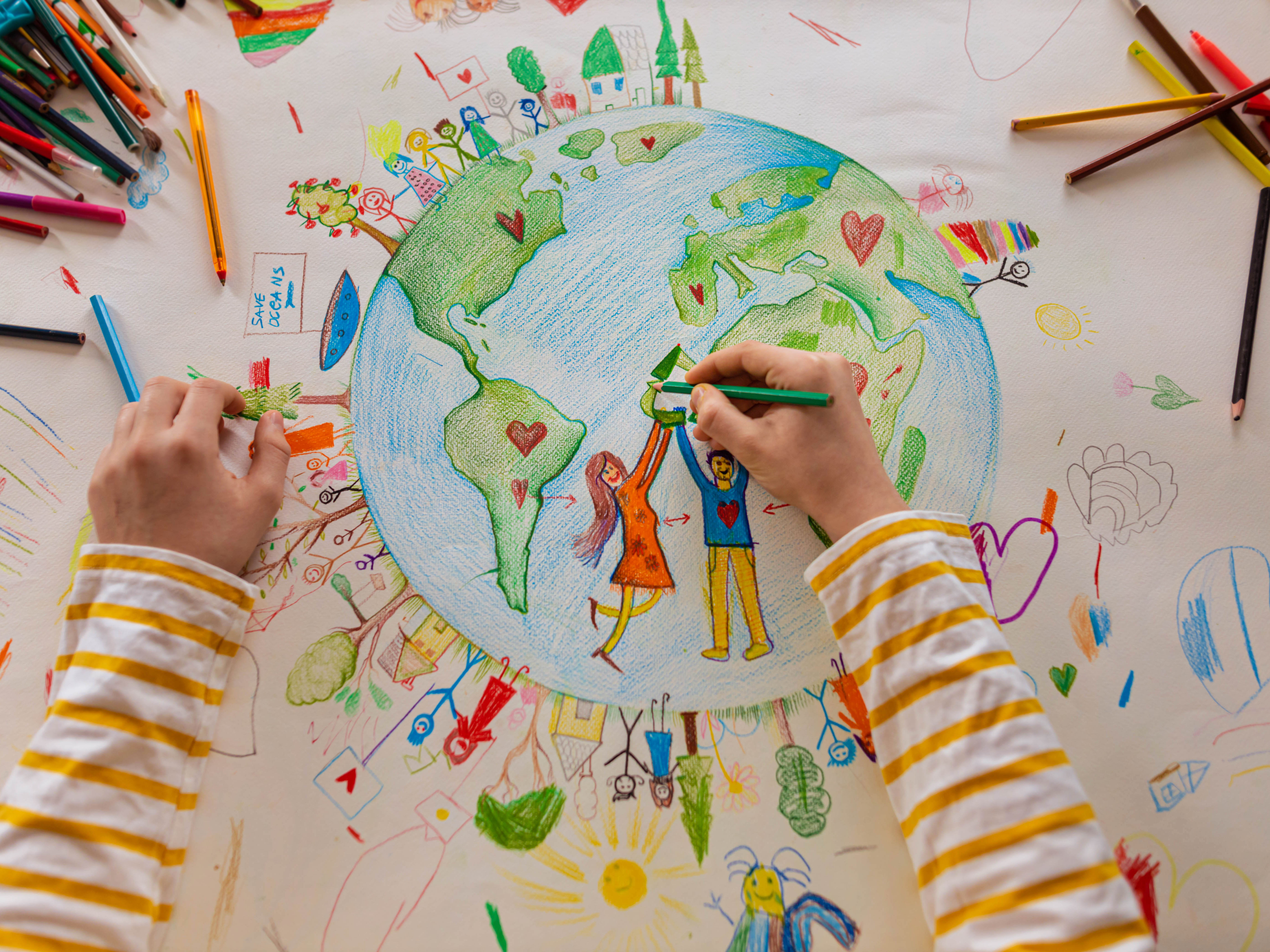 A child's hand drawing planet Earth with colourful pens