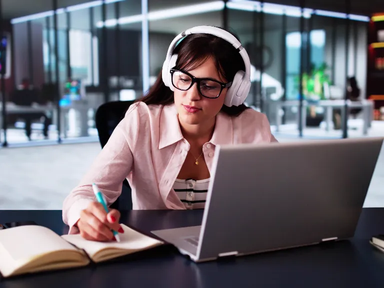 a woman wearing headphones and writing on a notebook