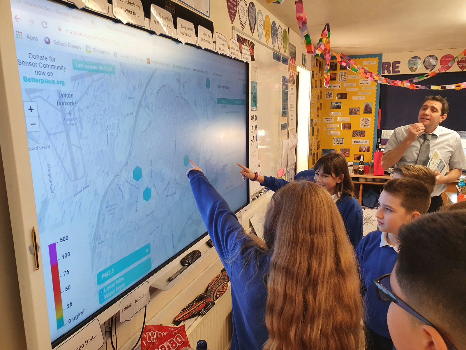 School children, supervised by a teacher, point to locations on a projected map. 