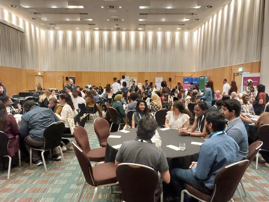 The cohort sits around circular tables in a large conference room