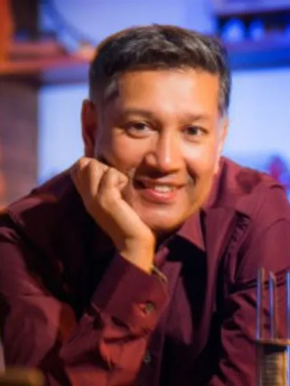 Professor Saiful Islam with his hand on his chin, wearing red shirt and smiling for camera
