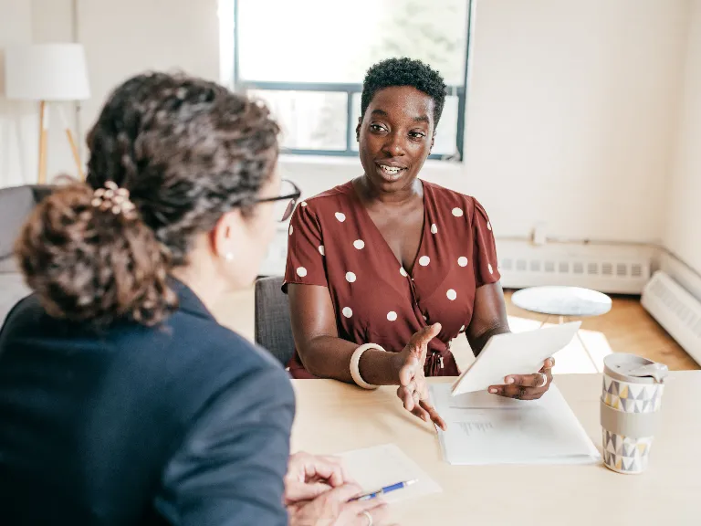Two women sat in an office setting and discussing with a notepad in hand