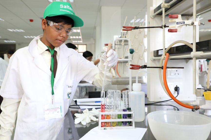 A boy holds a pipette over a series of test tubes filled with multi-coloured liquid A boy holds a pipette over a series of test tubes filled with multi-coloured liquid