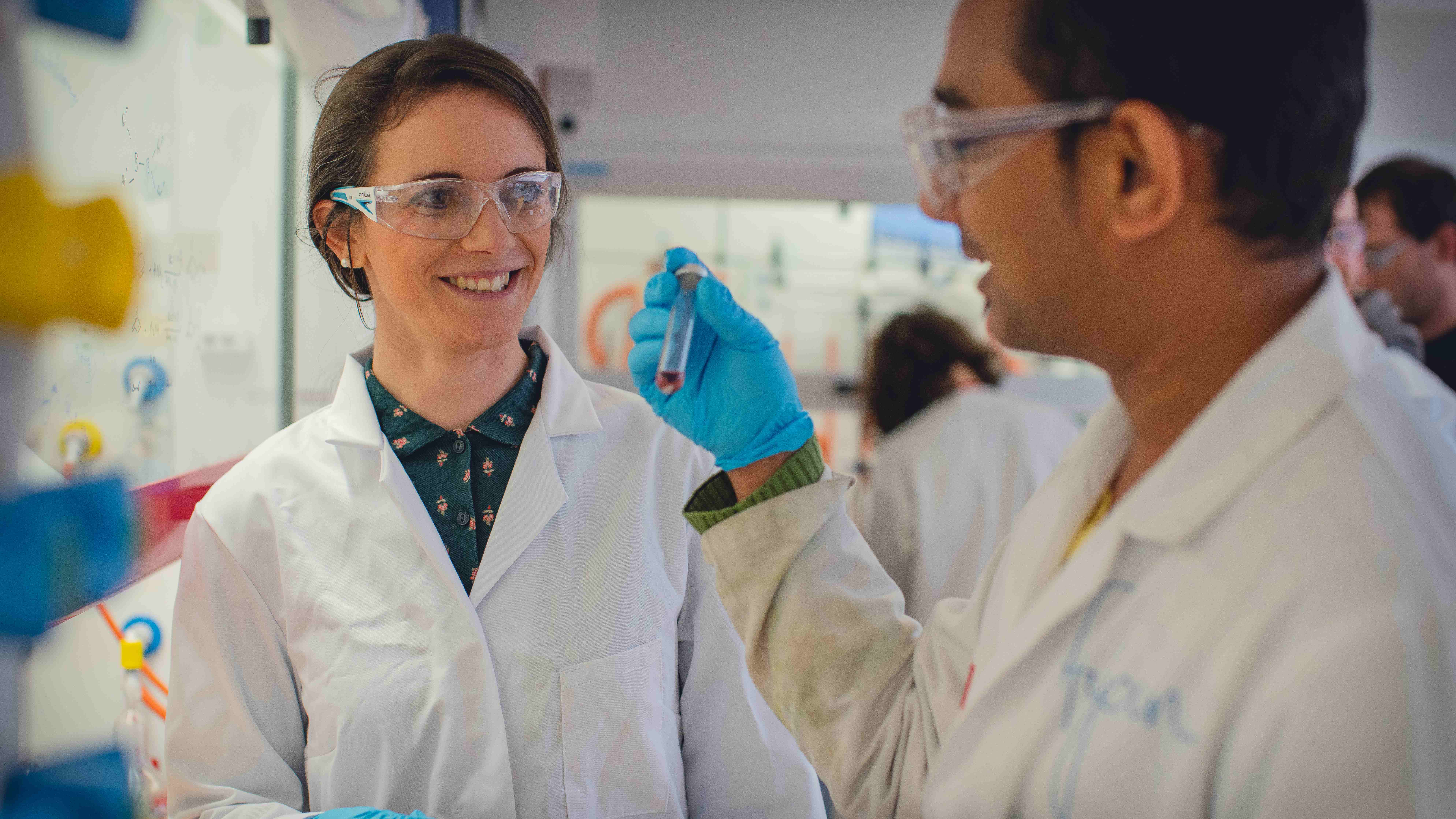 Professor Rebecca Melen with one other, in lab coats holding a tube of liquid
