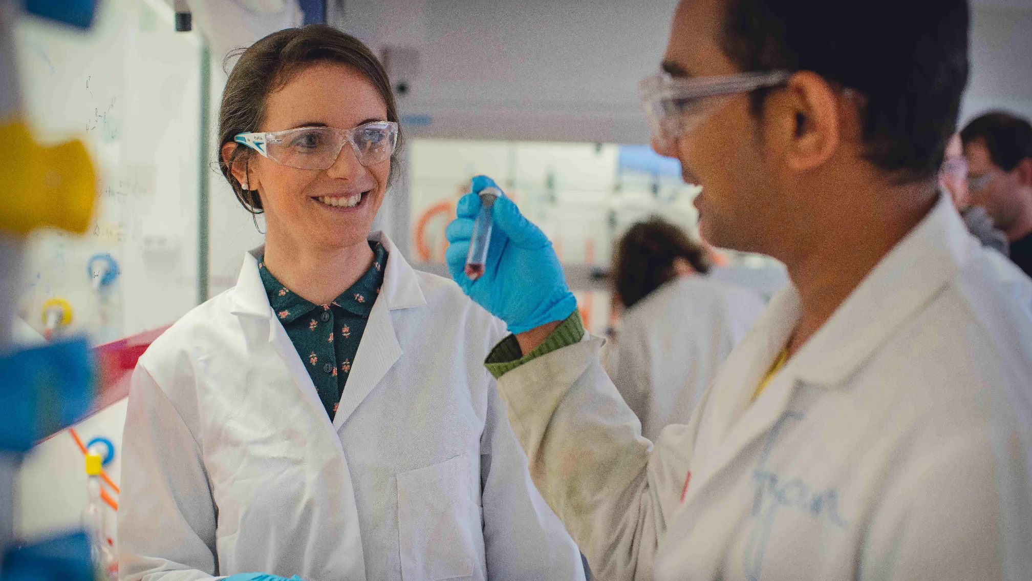 Professor Rebecca Melen with one other, in lab coats holding a tube of liquid