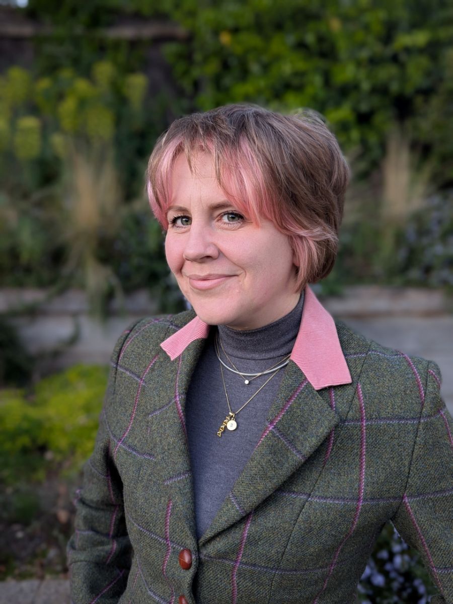 Dr Zoё Waller with pink hair wearing a green jacket with pink collar