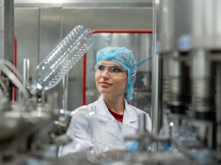 A female lab technician wearing white coat and blue hairnet in a lab