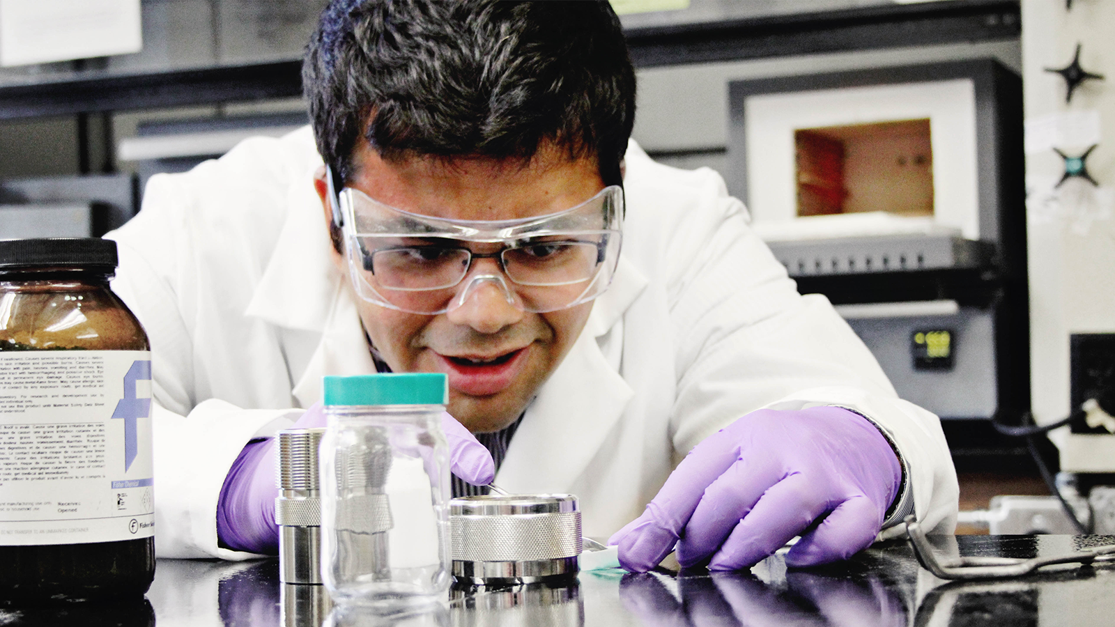 Professor Sarbajit Banerjee wearing goggles and gloves looking closely at objects on a lab bench
