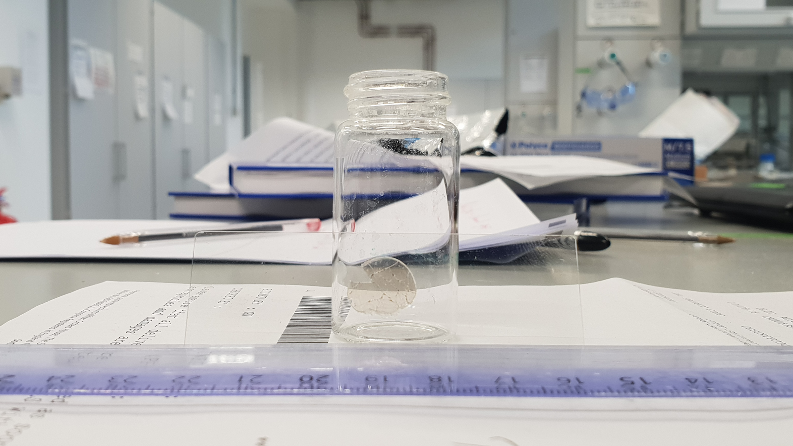 A glass jar on a table with papers containing data at the Pioneers in Hybrid Glass Research lab
