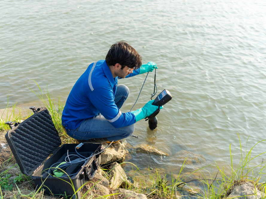 Man next to a lake holding water quality monitoring device in hand
