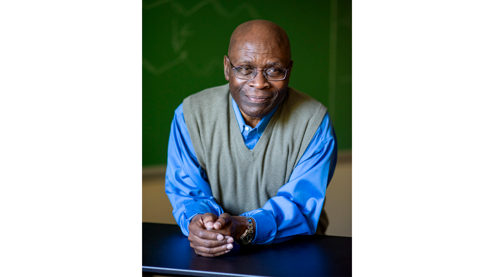 Professor Samson Jenekhe sitting at a desk in blue shirt and glasses, smiling for camera