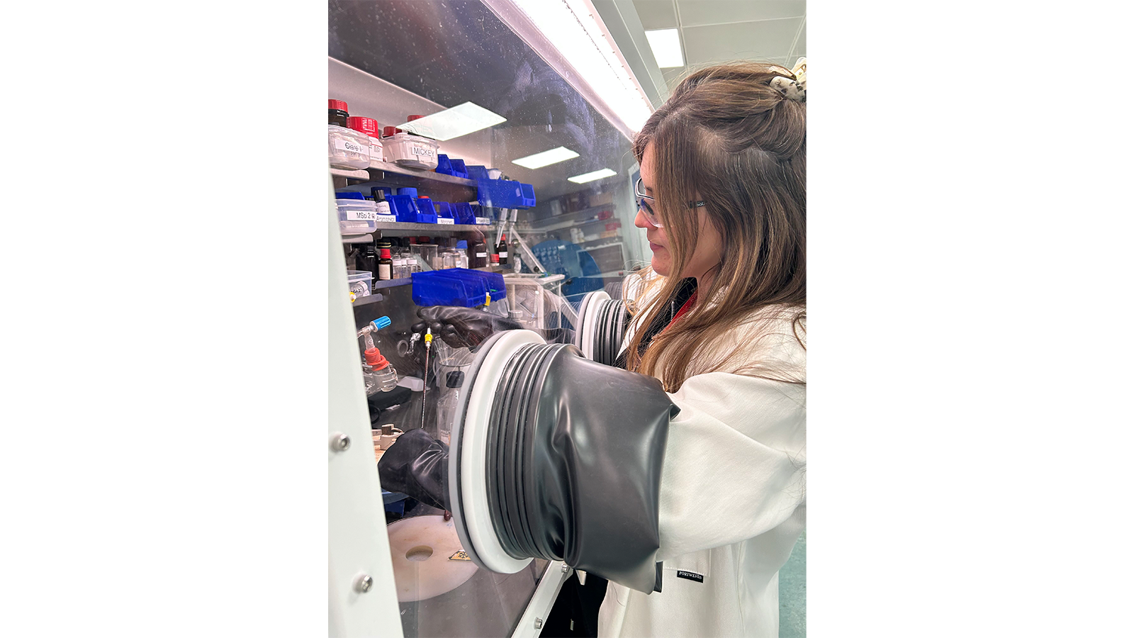 Dr Clare Bakewell wearing a white lab coat and using glove box