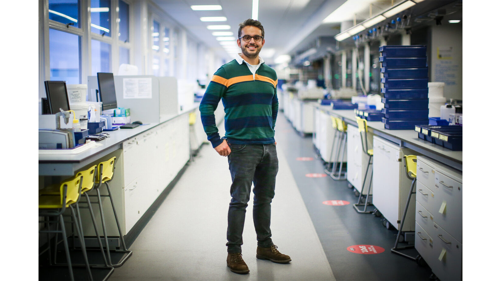 One of the team standing in a room with white cabinets and a green and orange striped rugby style shirt