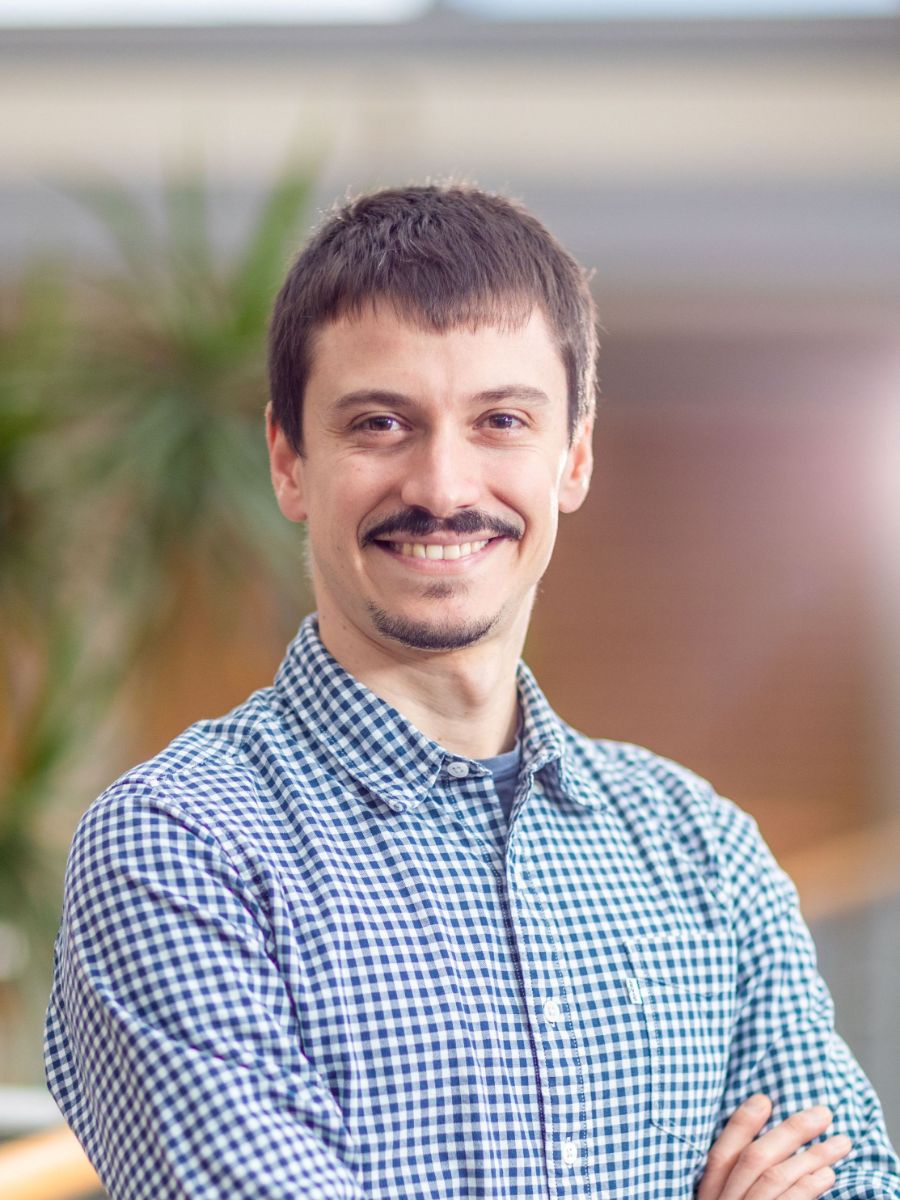Dr Mattia Silvi with moustache smiling at camera, in blue check shirt