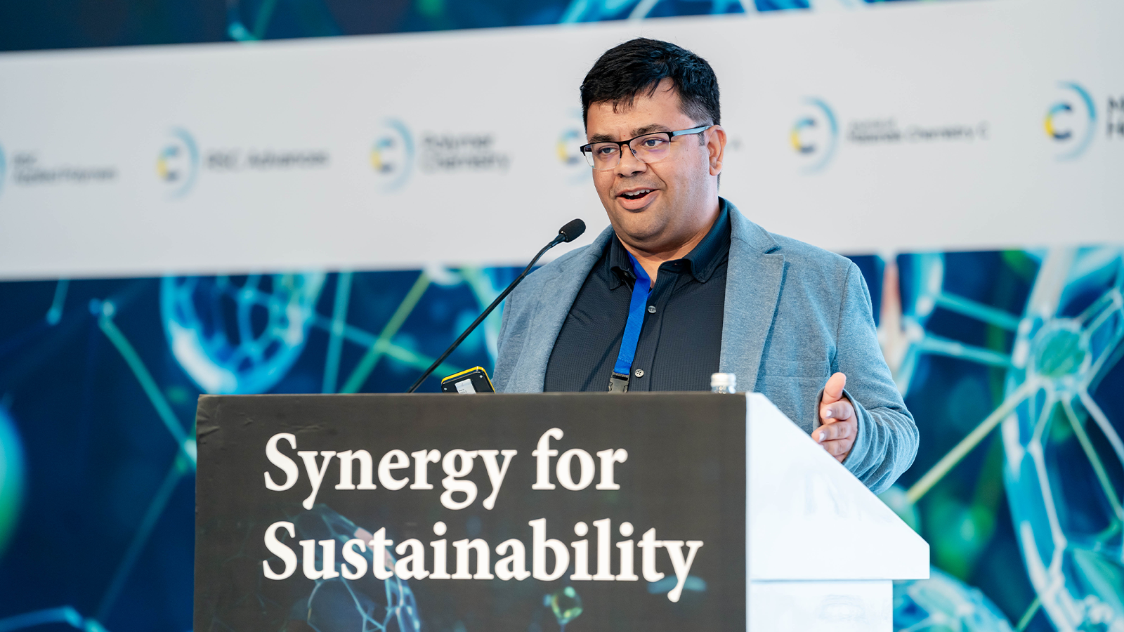 Professor Sarbajit Banerjee standing at a podium marked "Synergy for Sustainability"