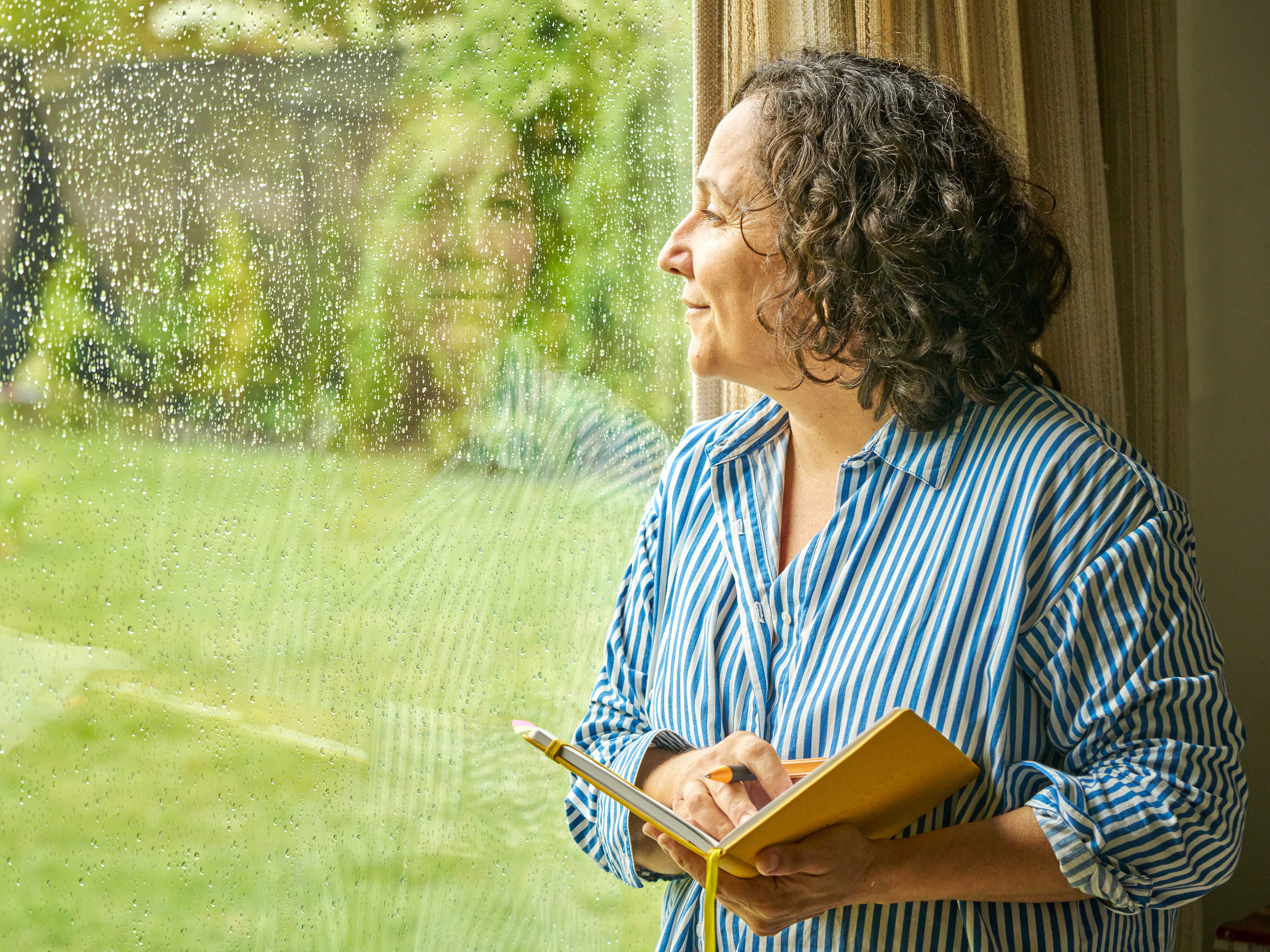 A woman with book in her hand looking out of the window