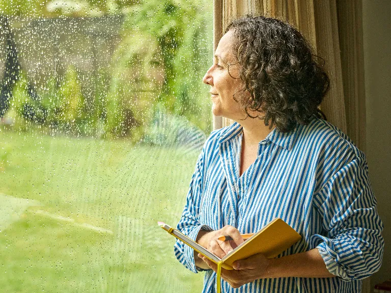 A woman with book in her hand looking out of the window