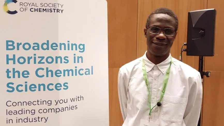 Professor Robert Mokaya stands next to a white Broadening Horizons banner and smiles