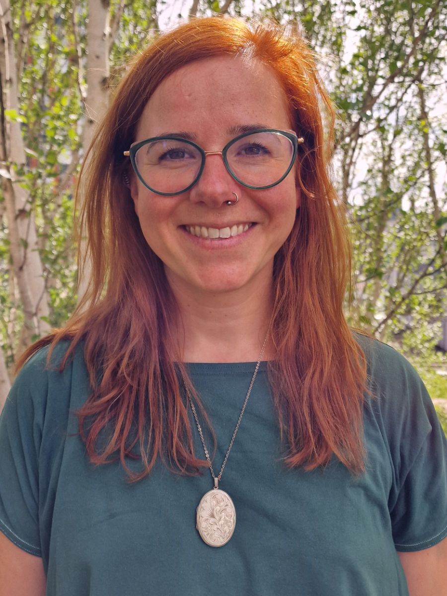 Dr Rebecca Beveridge with long red hair wearing glasses green top and a necklace, smiling for camera