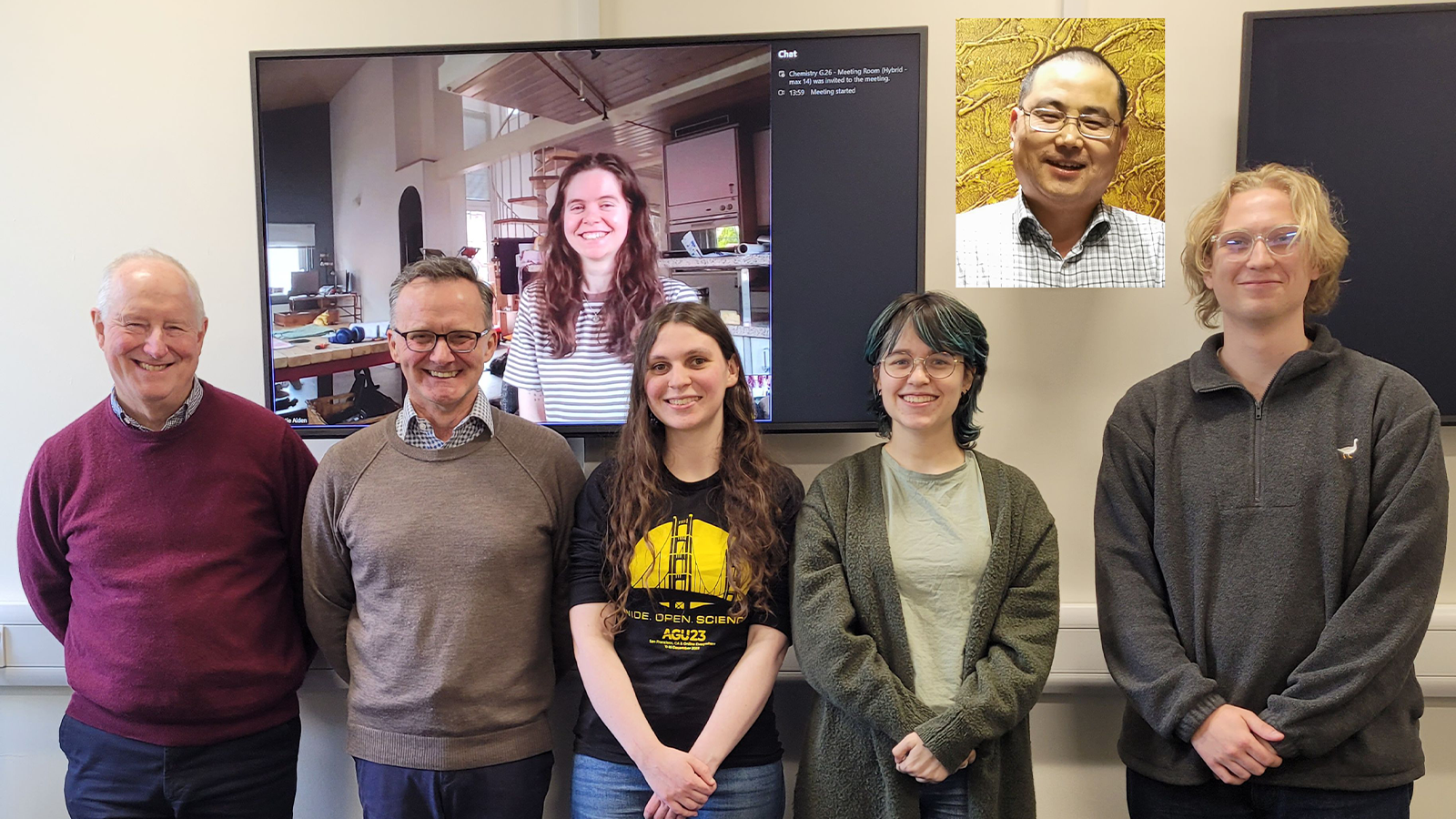Professor John Plane with a group of people standing in front of a large screen with zoom showing other colleagues