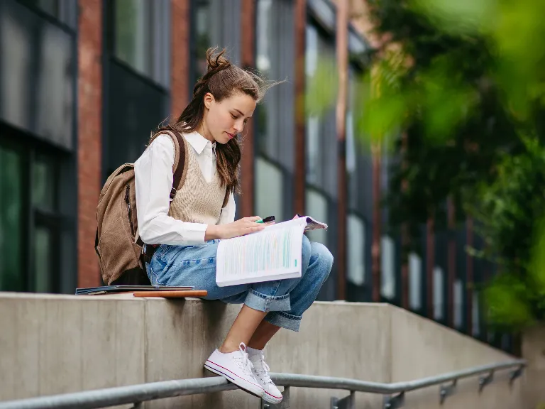 A college student sitting outside looking at her book