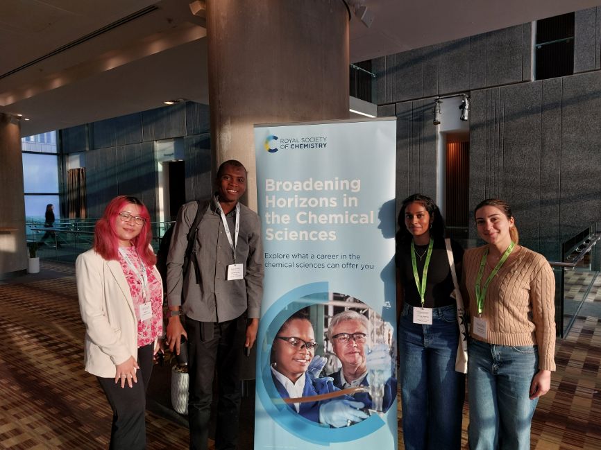 A group of four participants stand together, with two either side of a Broadening Horizons standing banner