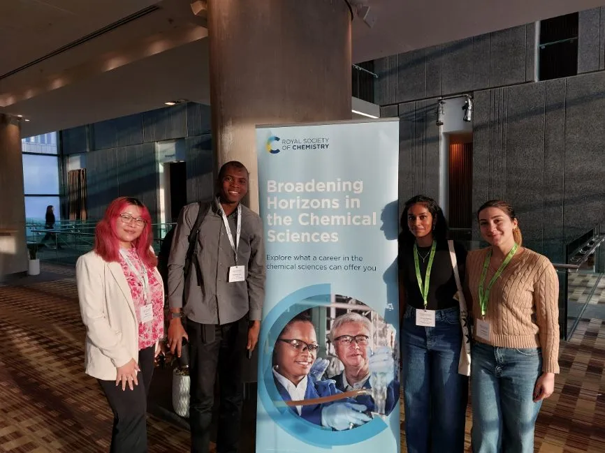 A group of four participants stand together, with two either side of a Broadening Horizons standing banner