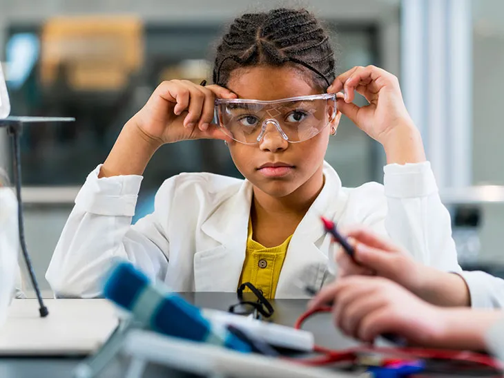 A child wearing safety glasses and a lab coat in a chemistry class