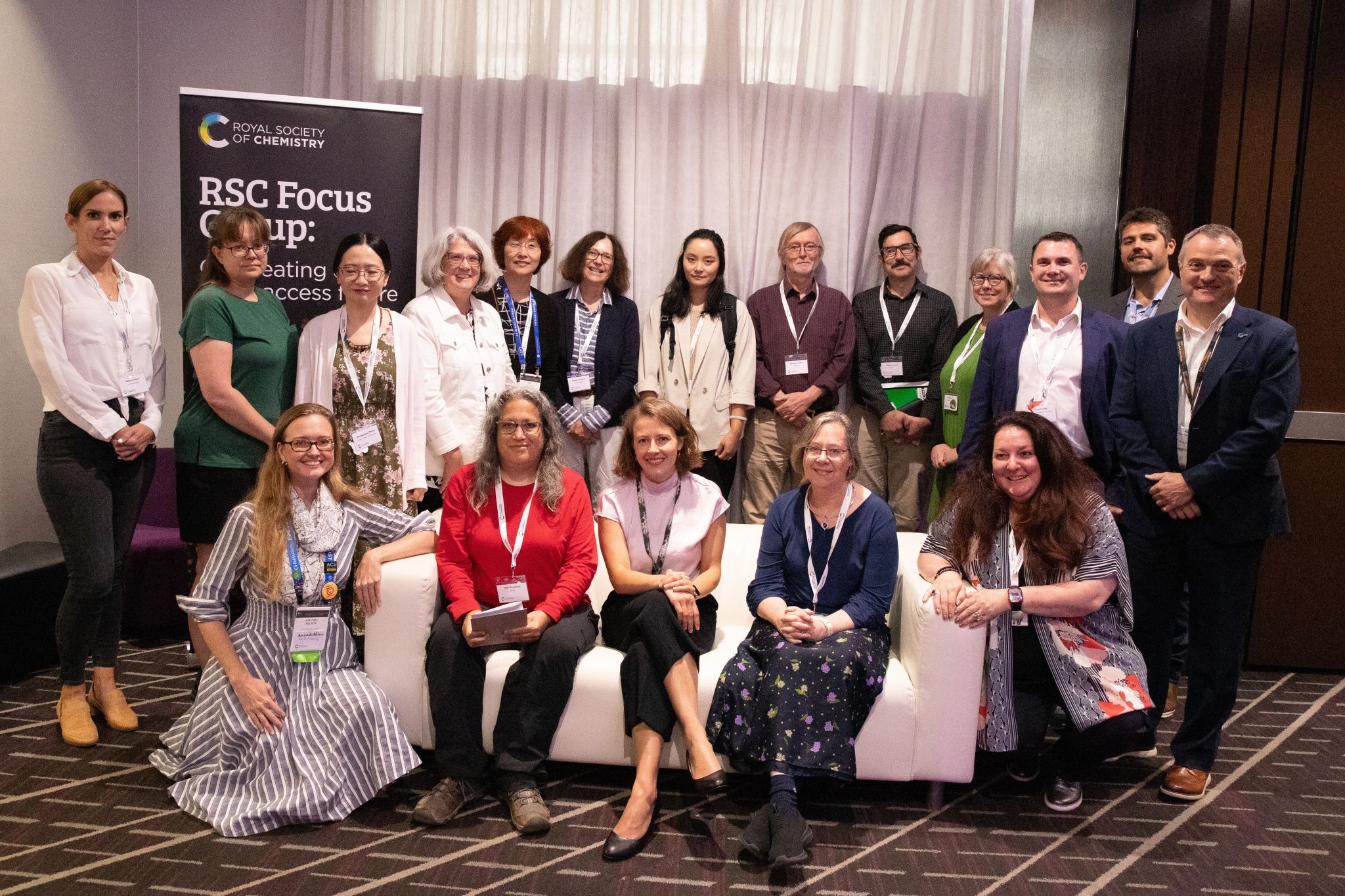 The Royal Society of Chemistry's Open Access transition focus group (13 people in the back row and five people down in front) poses together in front of an RSC banner in a conference room at an Am