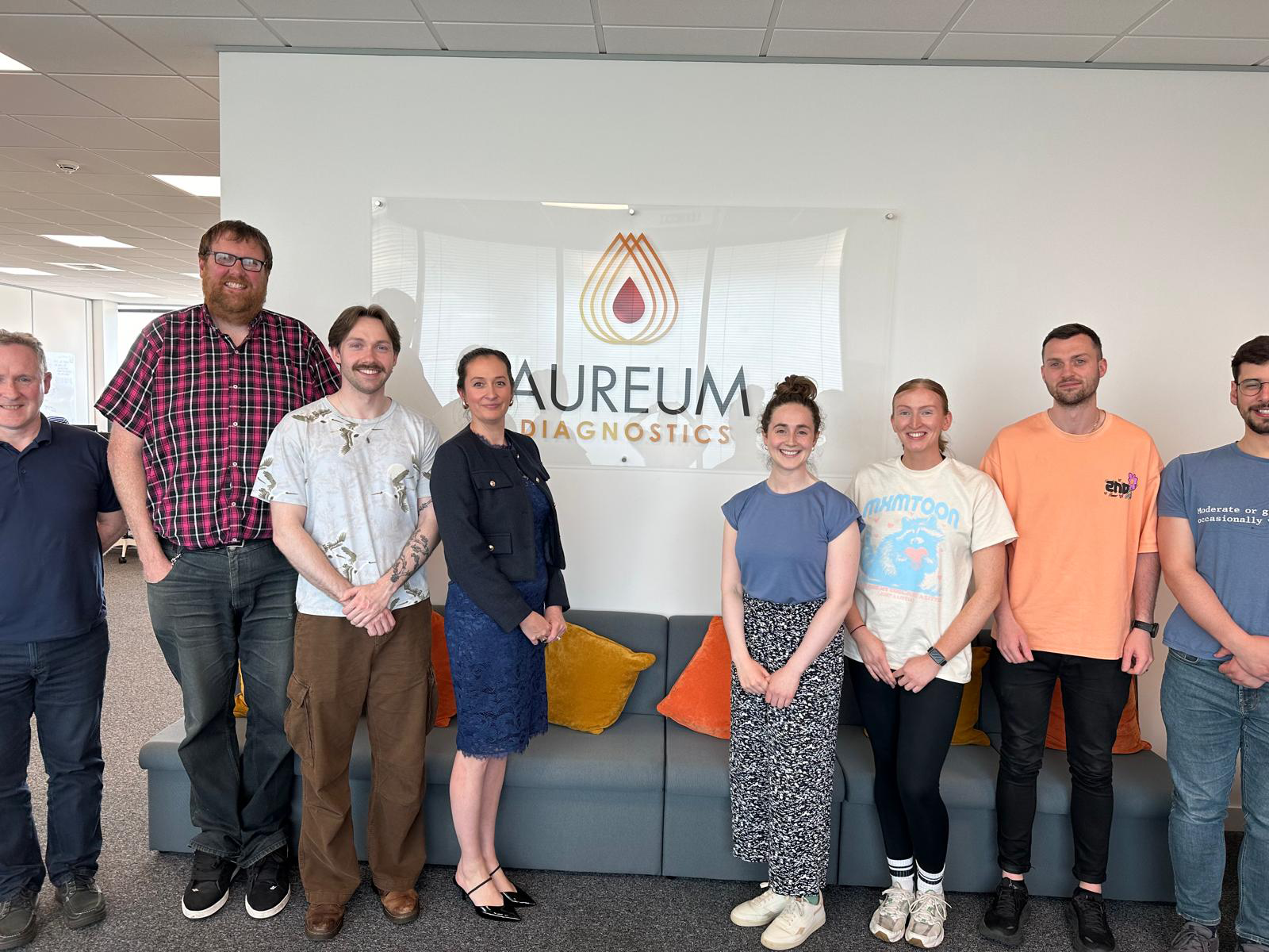 Professor Damion Corrigan and others facing camera in front of "Aureum" sign