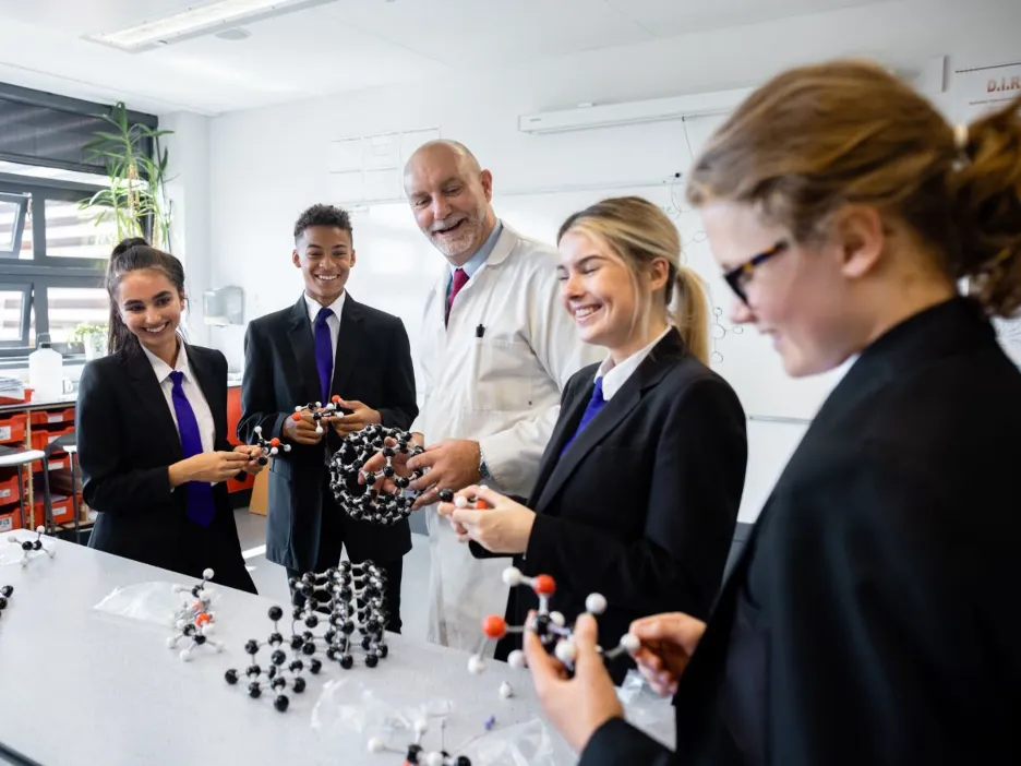 School children in uniform in classroom with teacher creating ball and stick models