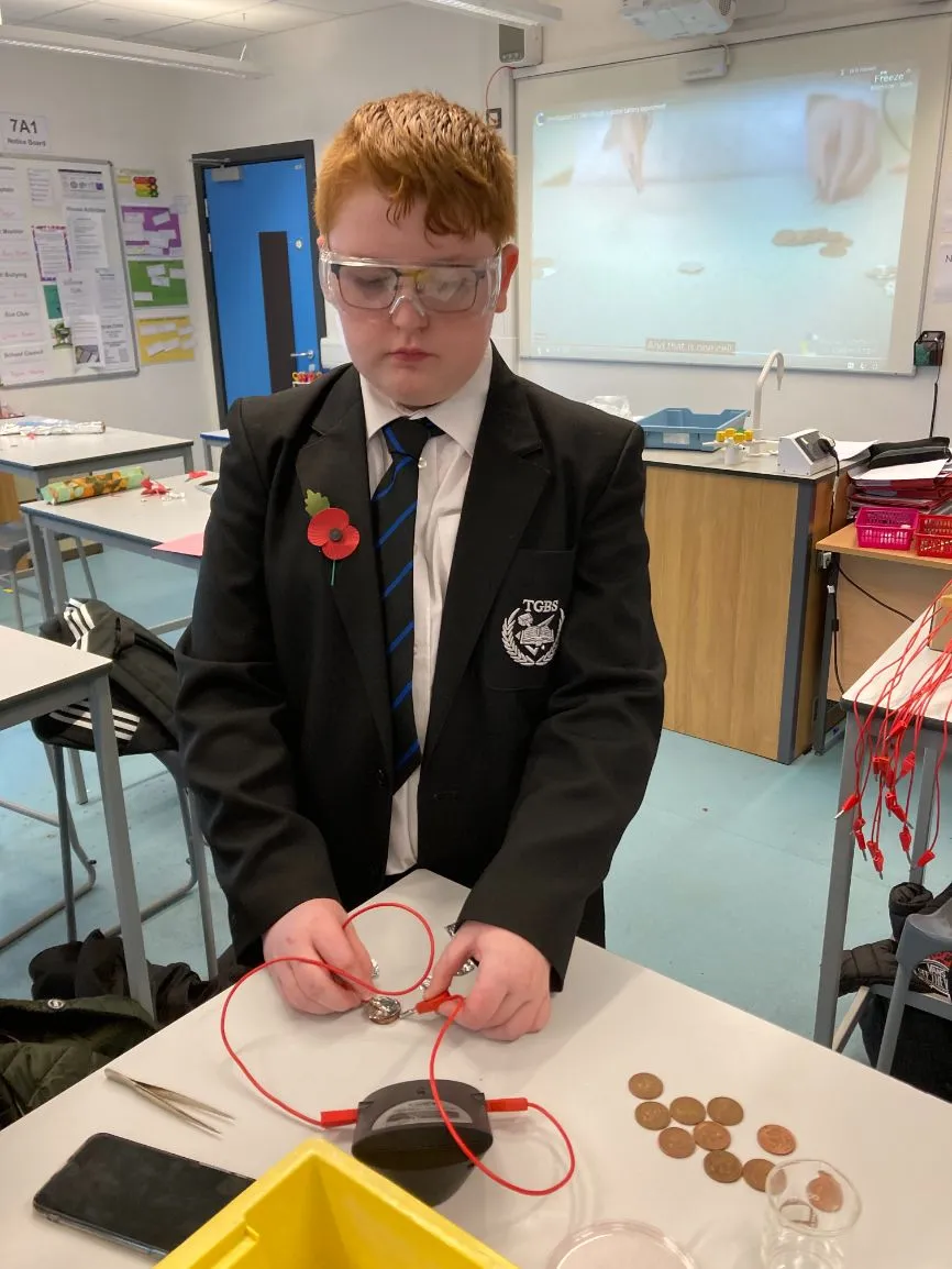 A boy wearing safety goggles conducts a battery experiment