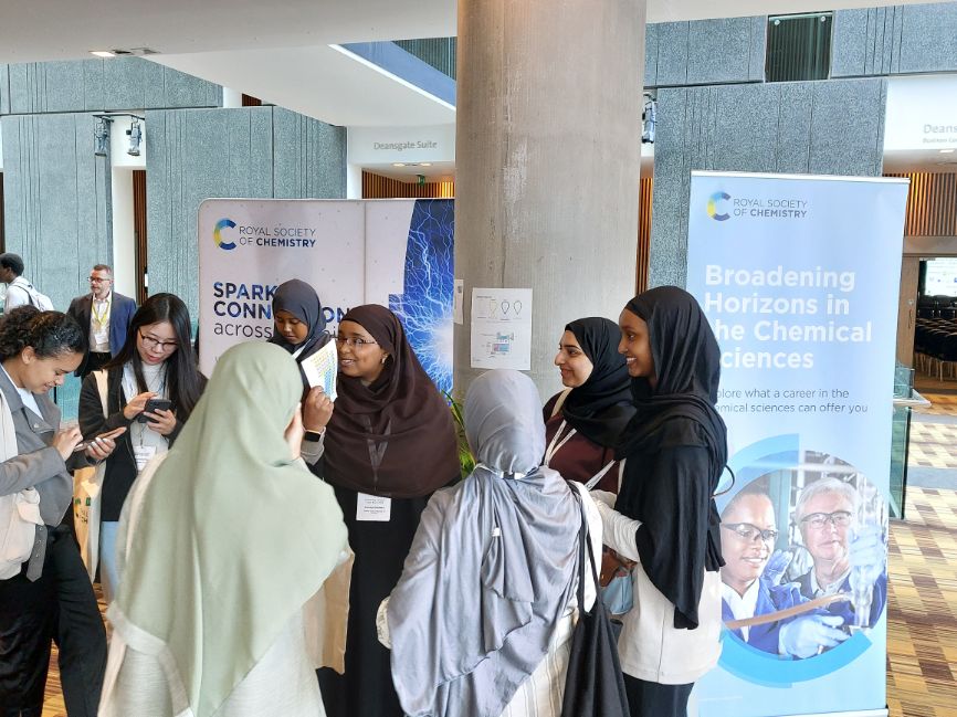 A group of women stand around a couple of RSC Broadening Horizons banners and talk