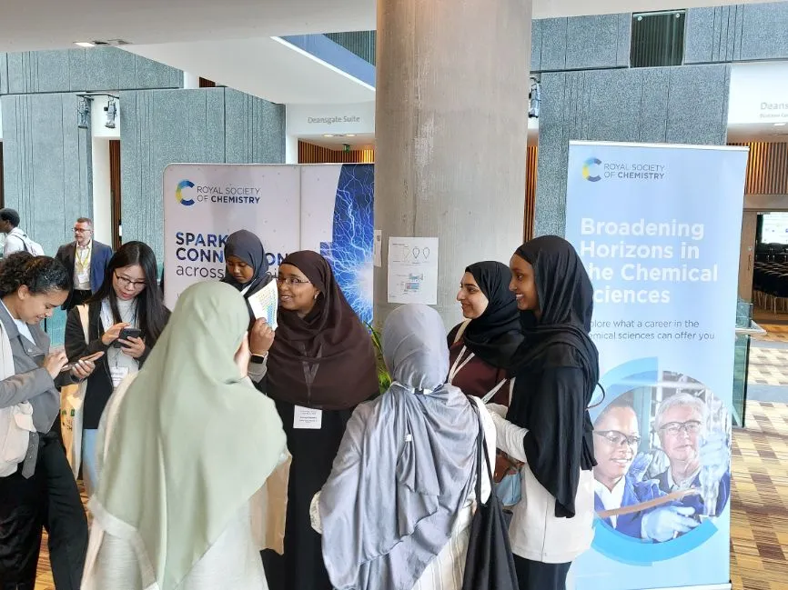 A group of women stand around a couple of RSC Broadening Horizons banners and talk