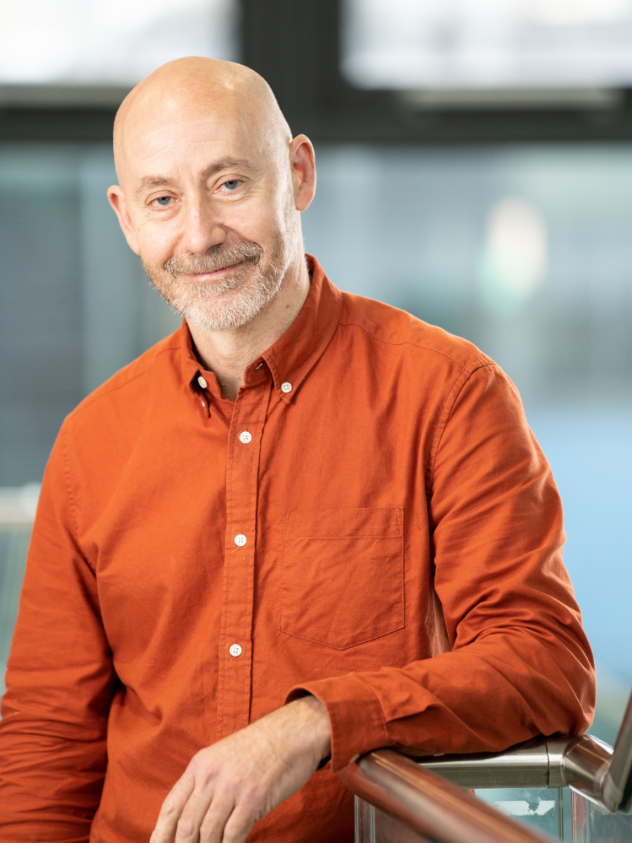 Professor Cameron Alexander in an orange shirt smiling for camera
