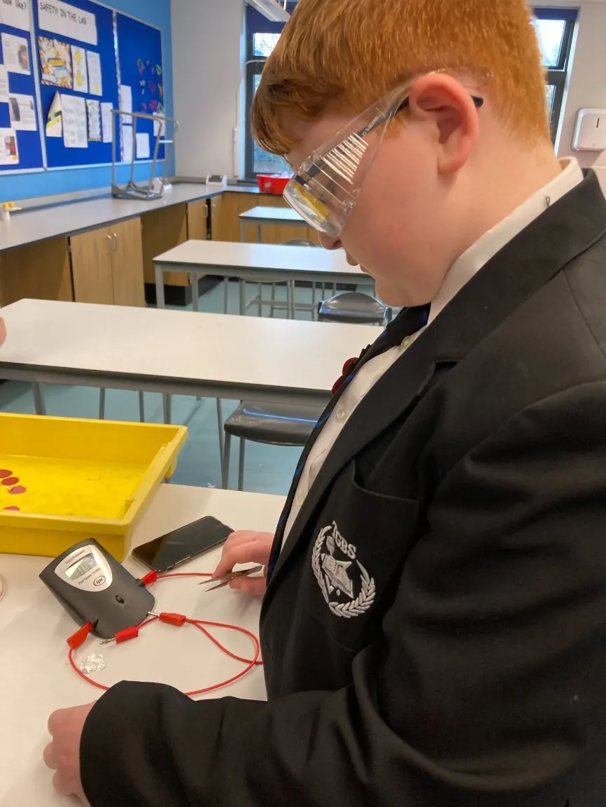 A boy wearing safety goggles conducts a battery experiment.
