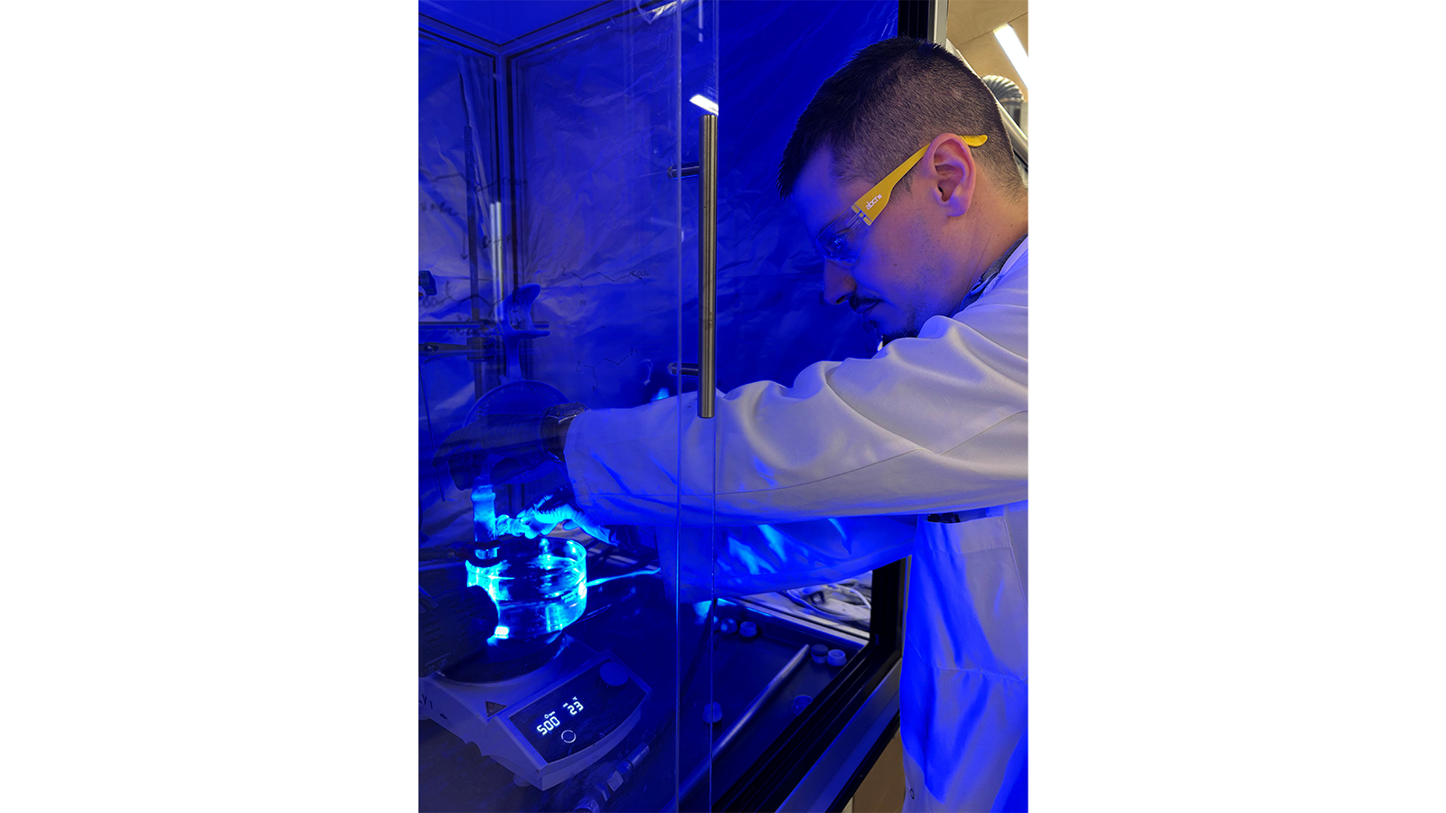 Dr Mattia Silvi wearing a white coat and goggles, working in blue light