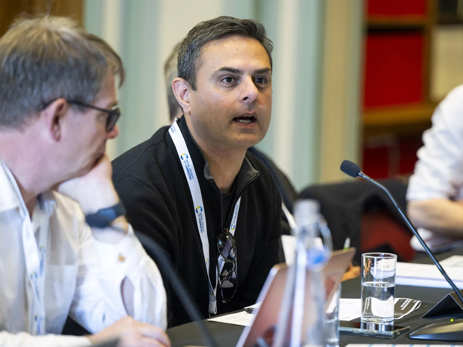 A judge sitting at a table asks a question of the presenting groups, who are out of shot