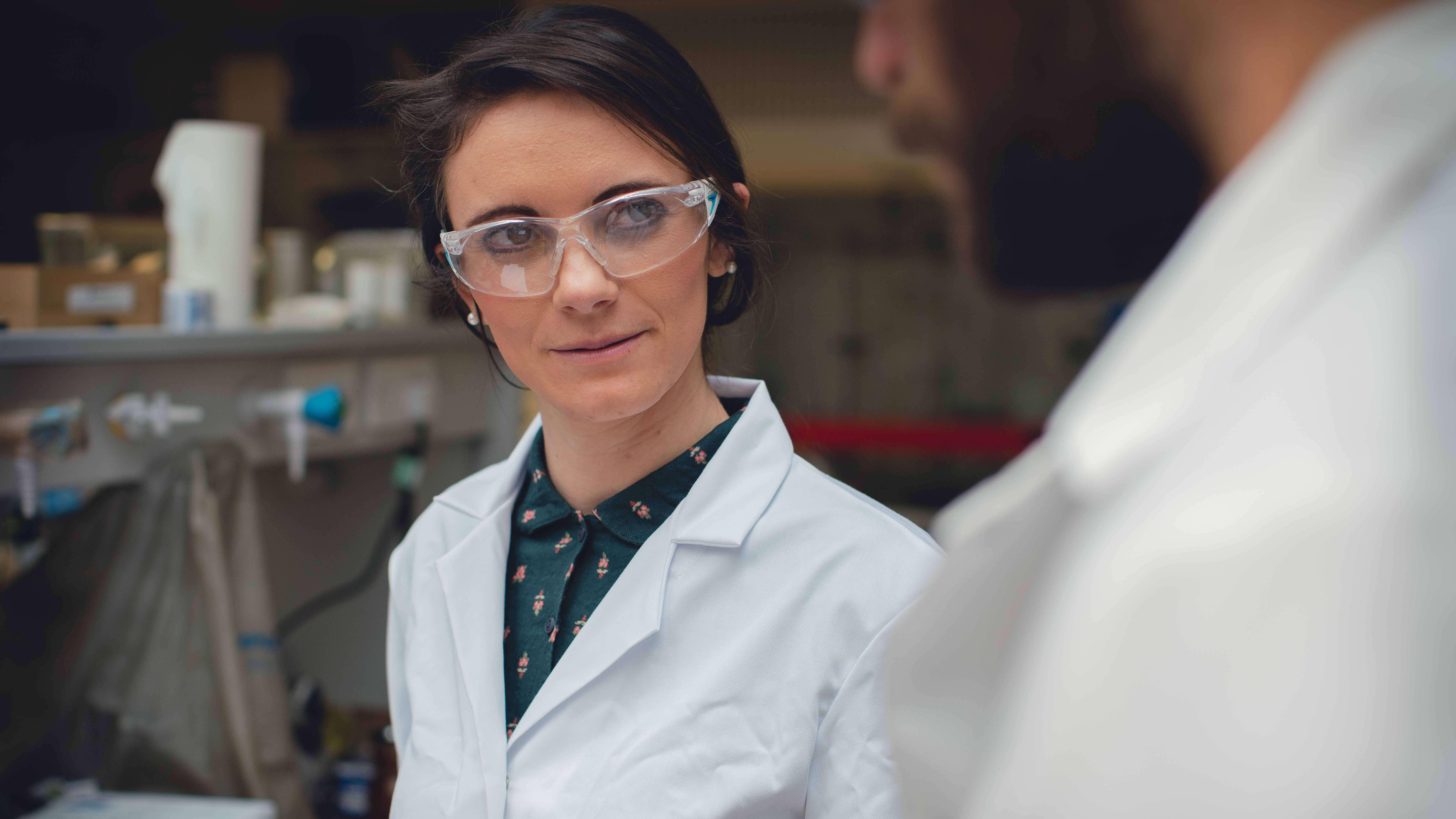 Professor Rebecca Melen wearing white lab coat and goggles in lab