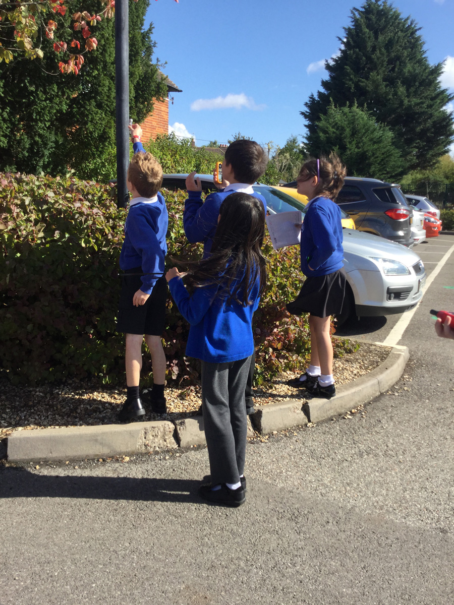 Primary school children in uniform standing outdoors and holding up a device to test the air.