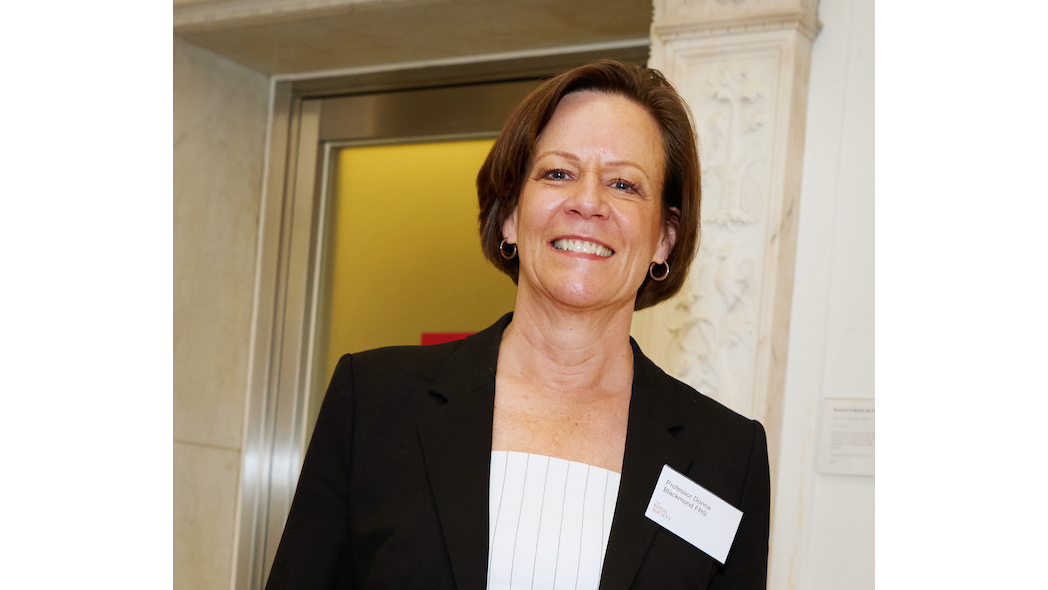 Professor Donna Blackmond in black suit jacket smiling at camera