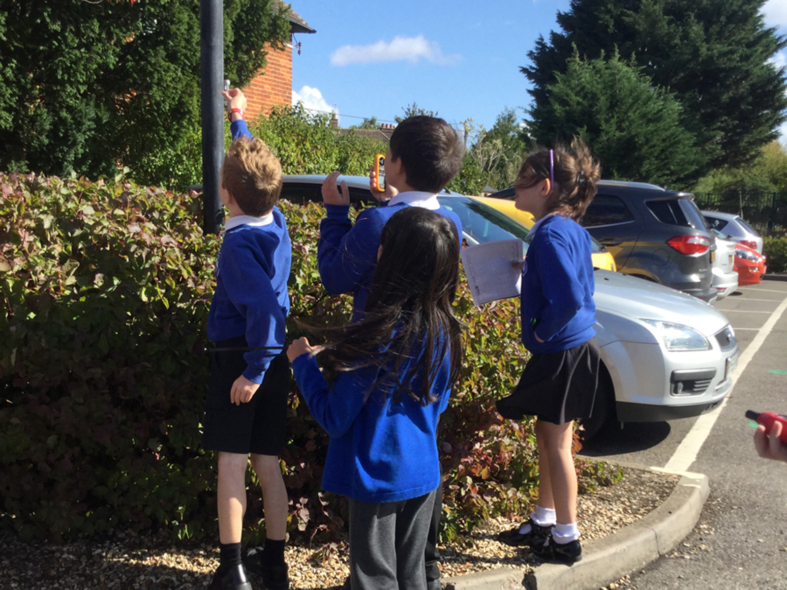 Primary school children in uniform standing outdoors and holding up a device to test the air.