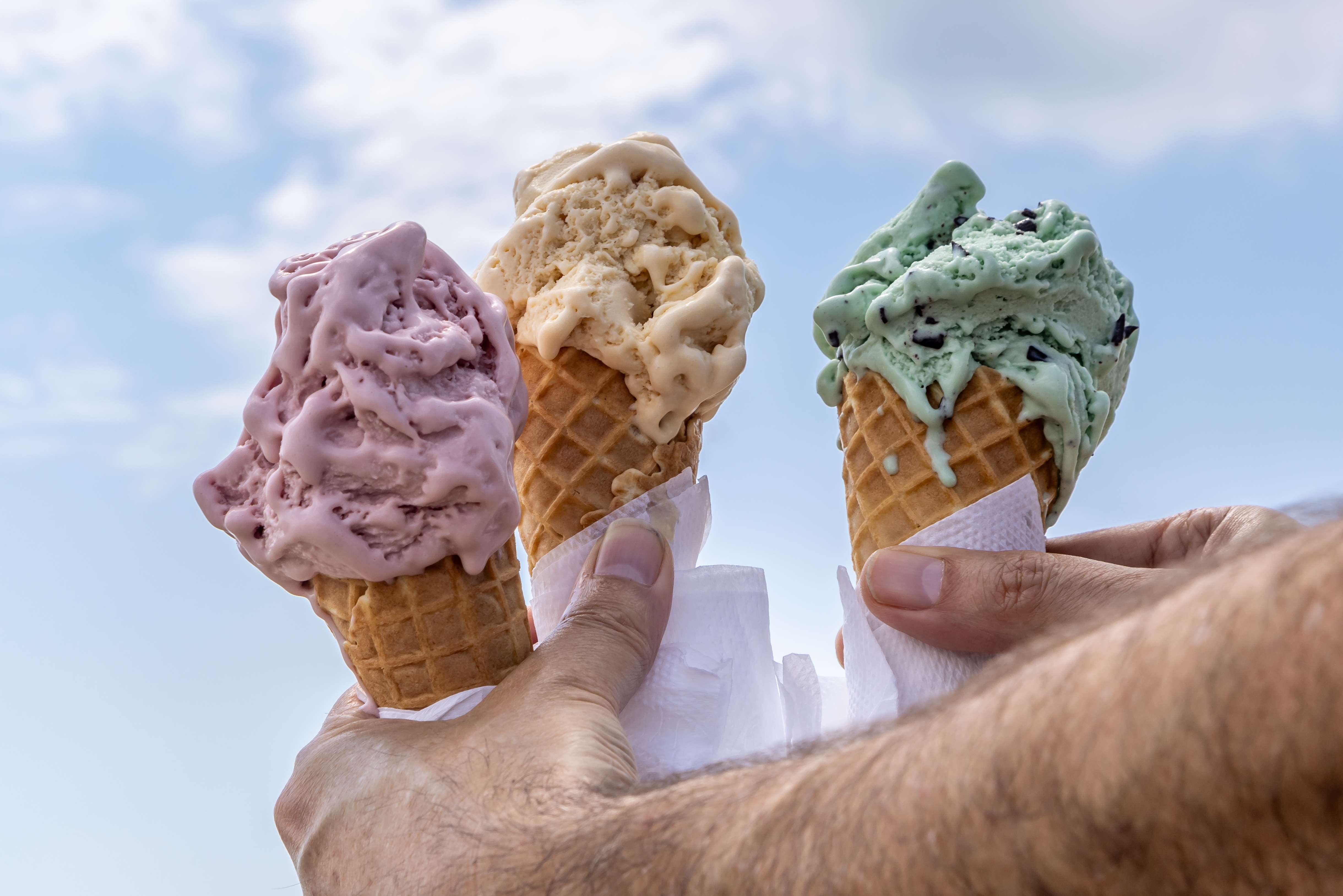 A picture of three ice cream cones - strawberry, vanilla maybe, and mint choc chip - being held by a hand from a body off screen. A picture of three ice cream cones - strawberry, vanilla maybe, and mint choc chip - being held by a hand from a body off screen.