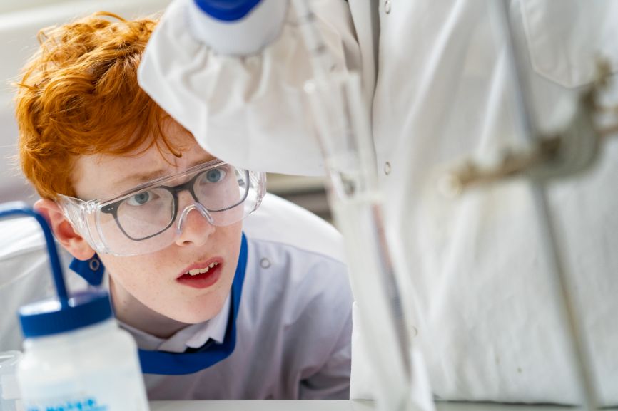 A redheaded student wearing safety goggles watches an experiment