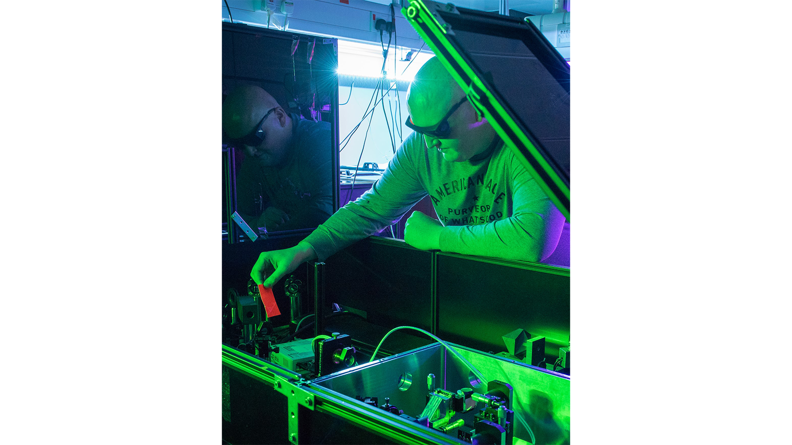 Dr Jack Woolley working on a machine in green light and wearing black safety goggles