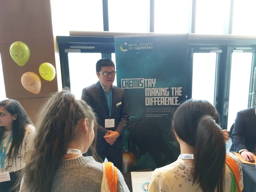 A member of the RSC team speaks with a couple of young women who have approached an exhibition stand while a banner in the background reads Chemistry Making the Difference