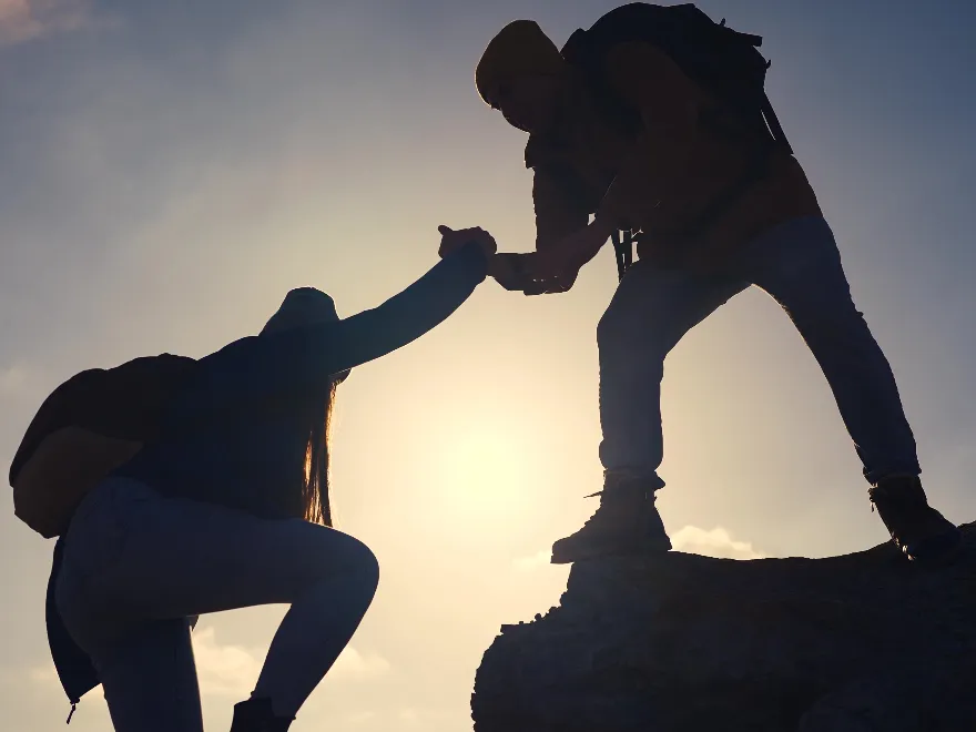Silhouette image of a person lending a helping hand to climb a rock or mountain